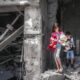 Palestinian children walking out of their destroyed home with their toys