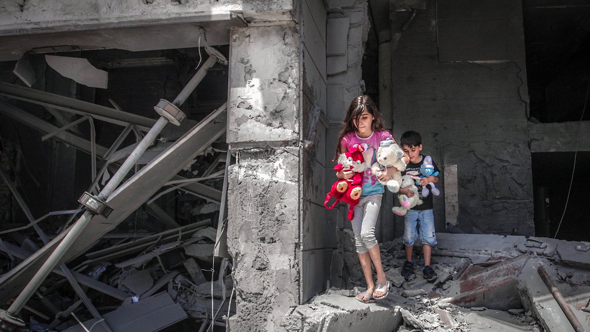 Palestinian children walking out of their destroyed home with their toys